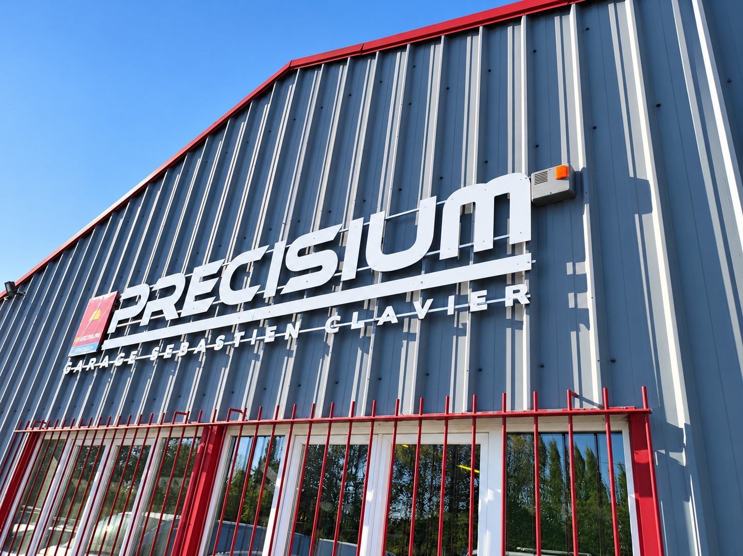 Façade du garage Precisium avec enseigne en lettres blanches sur bardage métallique